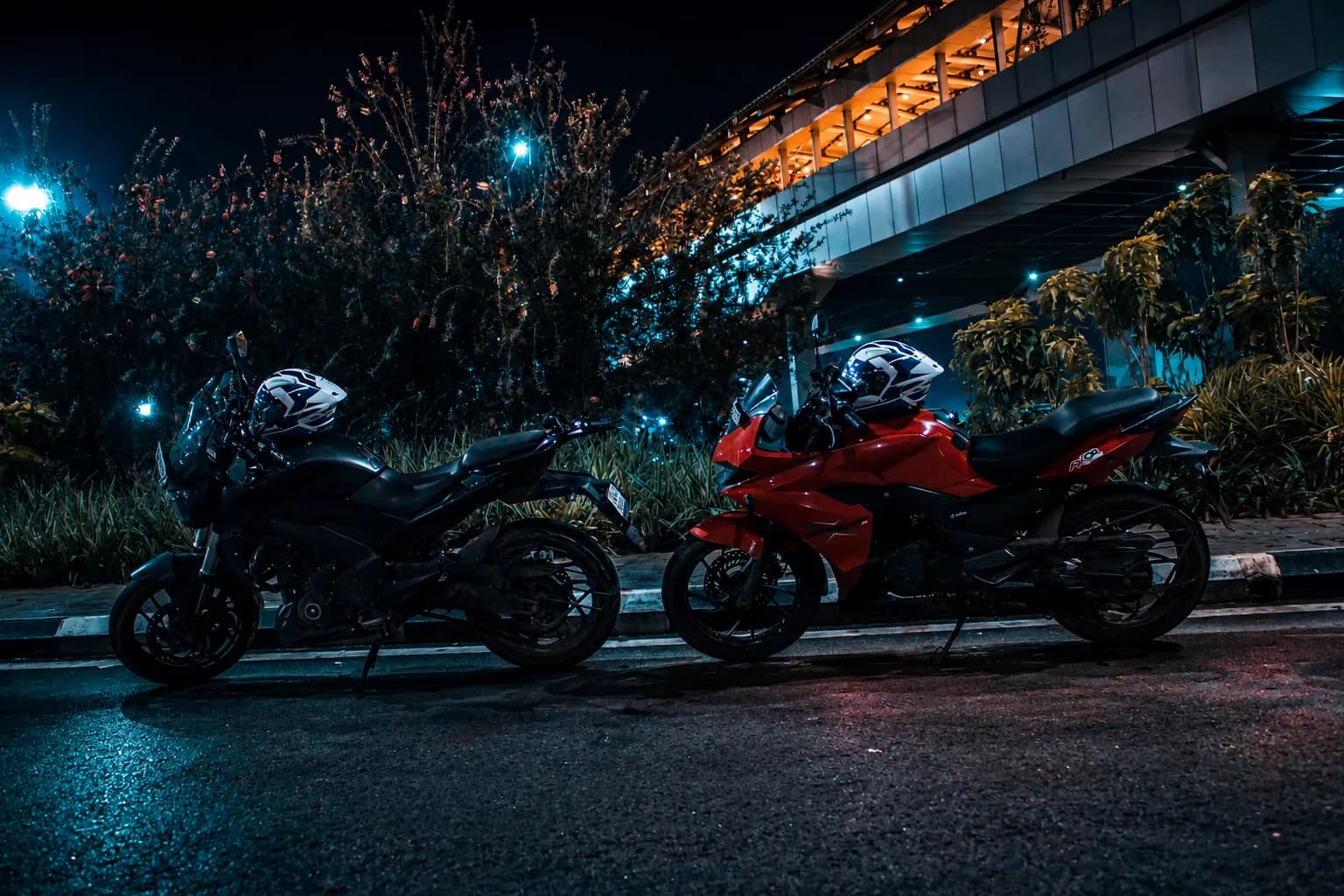 Two motorcycles parked on a dark roadside beneath an elevated metro line at night.