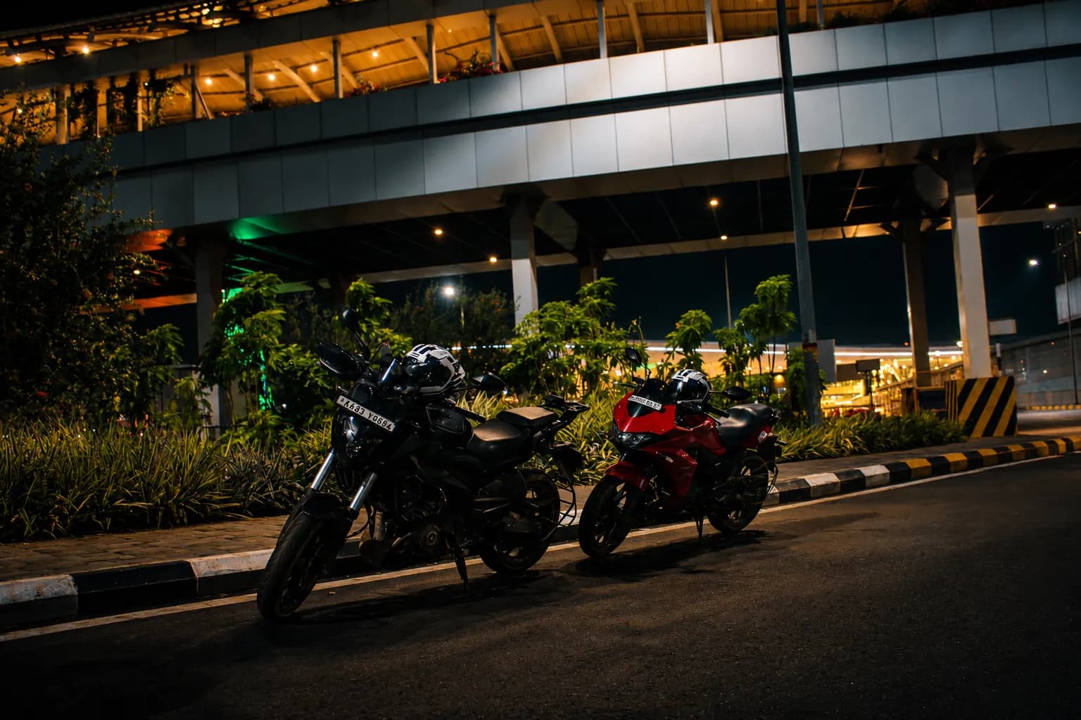 Two motorcycles on a curving road beneath a modern overpass at night.