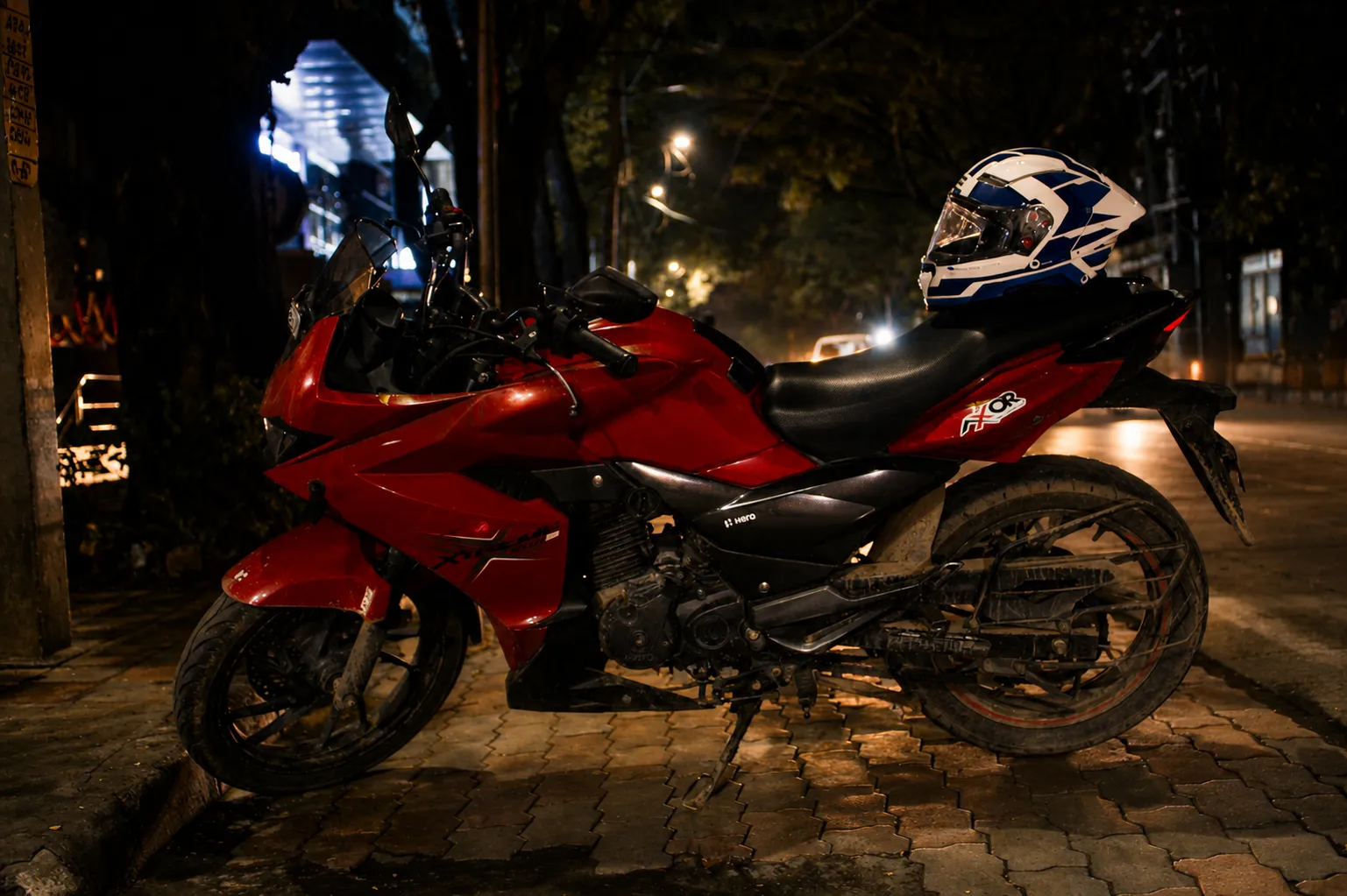 A red sportbike with a helmet on its seat, parked on a brick pavement at night.